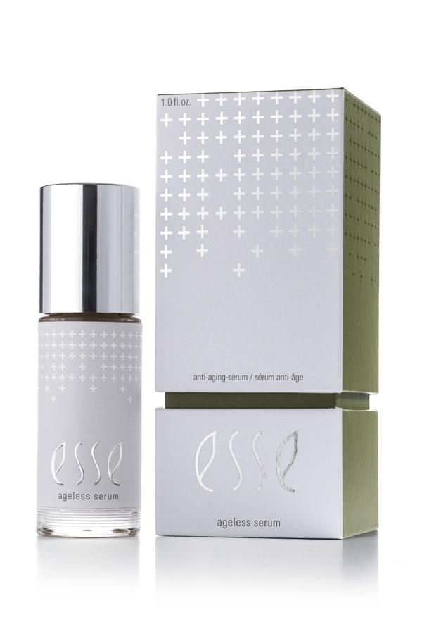 A bottle of Ageless Serum with a shiny silver cap stands beside its matching white and green box, both displaying minimalist silver text and cross designs.