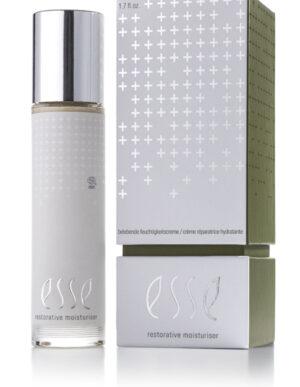 A bottle of Restorative Moisturiser with a silver cap stands beside its matching silver and green box, both decorated with white plus signs and featuring the product name in elegant lettering.