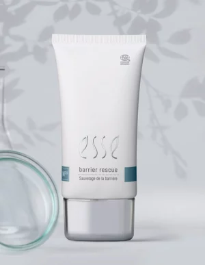 A white tube labeled “Import placeholder for 57617” stands upright with a silver cap. There are faint shadows of leaves and a glass object visible in the soft gray background.